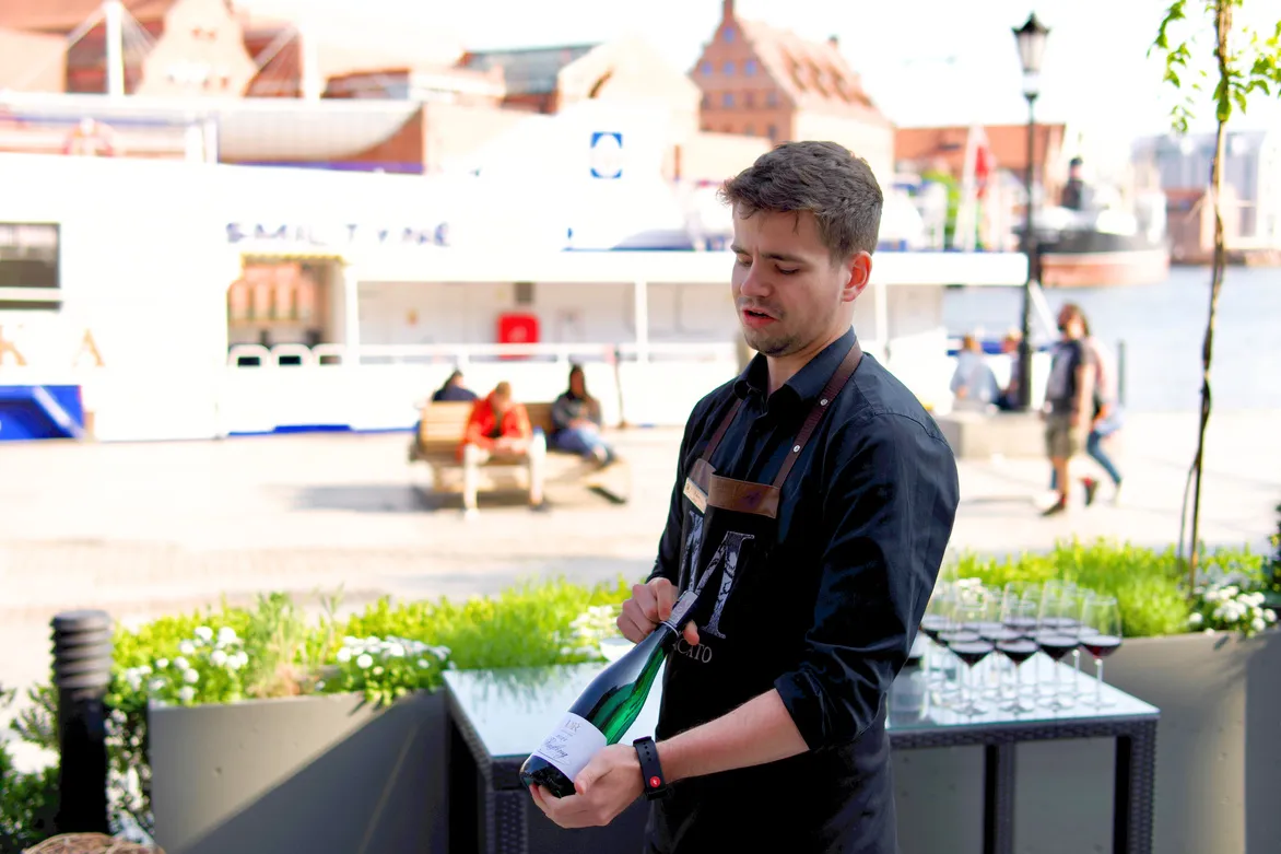 Sommelier trzyma w rękach butelkę wina, prezentując etykietę, opowiada o nim.